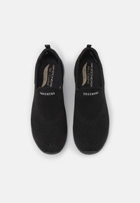Scarpe slip-on nere con tomaia in rete, caratterizzate da un design testurizzato, pannelli laterali elastici e il marchio "Skechers" sul davanti.
