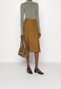 Brun houndstooth pennkjol med sidoflik, kombinerad med en ljusgrön polotröja och svarta loafers. Inkluderar en beige handväska.