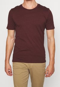 Bordeaux kortärmad t-shirt i mjukt tyg, med rund halsringning och en figurnära silhuett, kombinerad med ljusbeige byxor.