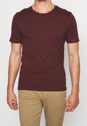T-shirt à manches courtes bordeaux en tissu doux, avec un col rond et une silhouette ajustée, associé à un pantalon beige clair.