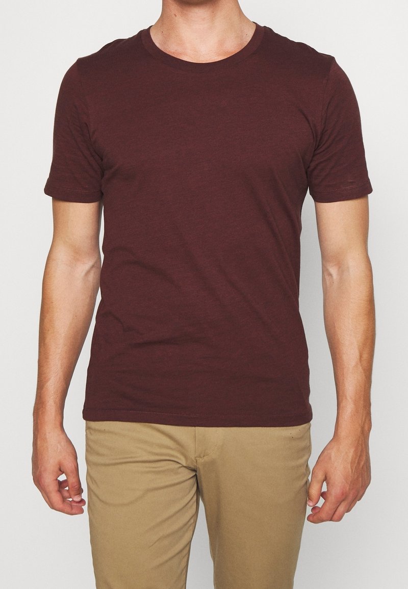 Bordeaux kortärmad t-shirt i mjukt tyg, med rund halsringning och en figurnära silhuett, kombinerad med ljusbeige byxor.