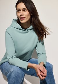 Sudadera azul clara con un cuello alto, textura suave y mangas largas, combinada con jeans azul claros, sentado en una pose relajada.