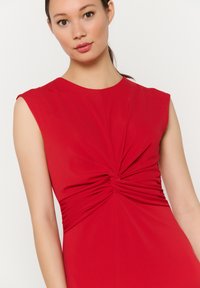 Vestido rojo ajustado con escote barco, mangas cortas y detalles fruncidos en la cintura, confeccionado en una tela suave y elástica.