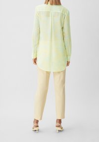 Blusa gialla a maniche lunghe, leggera, con motivo a foglie, abbinata a pantaloni gialli chiari e tacchi gialli con cinturini.