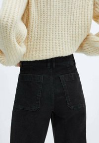 Jeans de mezclilla negros de cintura alta con dos bolsillos traseros, con un corte clásico y una textura de tejido resistente, combinados con un suéter de punto color crema.