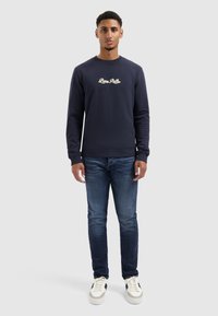 Navyblauwe sweatshirt met witte geborduurde tekst "Live Path" op de borst, gecombineerd met donkerblauwe spijkerbroek en witte sneakers. Soepele textuur.
