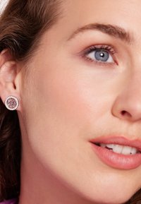 Zilverkleurige studoorbel met een ronde vorm en een bloemenpatroon, omringd door kleine heldere edelstenen, tegen een neutrale achtergrond.