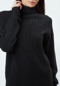 Schwarzer Rollkragenpullover mit strukturiertem Muster, erhöhten, diagonalen Linien sowie gerippten Bündchen und Saum für eine taillierte Silhouette.