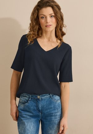 Marineblauwe V-hals top met korte mouwen, van textuurstof, gecombineerd met lichtblauwe jeans. Eenvoudig ontwerp met een ontspannen pasvorm.