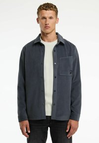 Jachetă din fleece de culoare gri închis, cu nasturi �în față, guler și un buzunar pe piept. Material texturat, asortat cu un pulover cu dungi de culoare deschisă dedesubt.