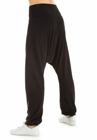Zwarte harem broek met een hoge tailleband, gemaakt van lichte stof, met een losse pasvorm, taps toelopende boorden en een subtiel logo-detail aan de zijkant.