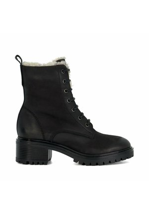 Zwarte leren enkelboot met een fluffy witte voering, ronde neus, vetersluiting aan de voorkant en een gestructureerde blokhak. Voorzien van een robuuste zool voor grip.