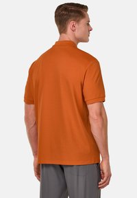 Polo tričko s krátkym rukávom v oranžovej farbe s klasickým límcom. Hladký, bavlnený materiál s voľným strihom. Viditeľné švy na švoch.