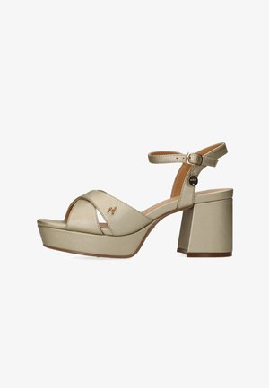 Goldfarbene Plateau-Sandalen aus Kunstleder mit einem breiten, gekreuzten Riemen, verstellbarem Knöchelriemen und einem klobigen Absatz. Mit einem Logo-Anhänger versehen.