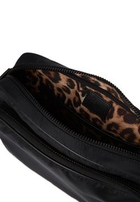 Sort nylon pung med lynlås, der har en indvendig leopardmønster-foring og et lille sort label. Glat tekstur med et stilrent design.