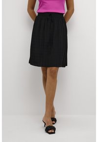 Falda negra con estampado y cintura con cordón, hecha de tela ligera. Combinada con una blusa rosa y sandalias de tacón negras.