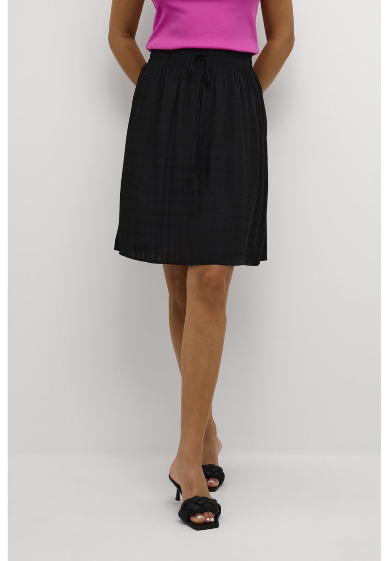 Falda negra con estampado y cintura con cordón, hecha de tela ligera. Combinada con una blusa rosa y sandalias de tacón negras.