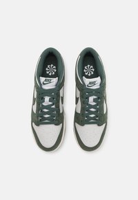 Nike sporta apavi ar zaļu zamšāda un baltu ādas augšdaļu. Iespējas ietver perforētu purngalu, zaļas saites un ziedu logo uz iekšējām zolēm.