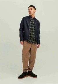 Dark blue zip-up jacket, black and green plaid shirt underneath, light brown corduroy pants, and black shoes with brown soles.