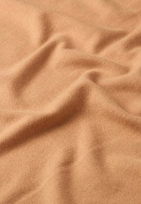 Tessuto marrone chiaro con una consistenza morbida, che mostra delicate pieghe e un sottile motivo a maglia. La superficie appare calda e accogliente.