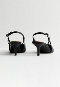 Sandales noires à talons avec un motif croco texturé, dos ouvert, sangle à la cheville avec une boucle en or, et un talon aiguille fin.