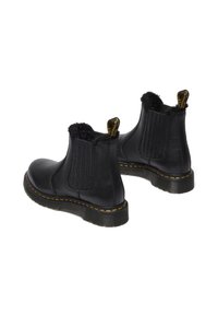 Botas de cuero negro hasta el tobillo con paneles laterales elásticos, superficie texturizada, forro de piel suave y costuras amarillas en la suela de goma.