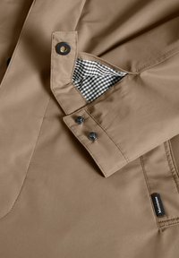 Beige waterproof jacket with snap buttons, featuring a checkered pocket interior detail and smooth, textured fabric.