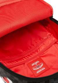 Borsa a scacchi nera con un interno di un rosso vivace. La fodera testurizzata presenta una tasca con zip e un'etichetta con i dettagli del prodotto.