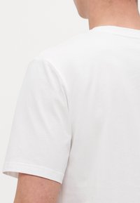 Hvitt bomulls T-skjorte med korte ermer, rund hals og en glatt tekstur. Har et rent, minimalistisk design uten synlige mønstre.
