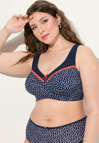 Sinih bras ja sobrade komplekt, millel on valge ja punane täppmuster, korallisooned ja väike pael keskel. Sile tekstuur.