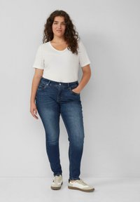Blauwe denim jeans met een slim fit, vijf zakken en een middelhoge taille, gecombineerd met een witte V-hals T-shirt en beige sneakers.