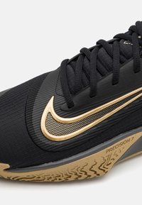 Czarne buty sportowe z teksturowanej tkaniny, złotymi akcentami, wyraźnym logo Nike oraz gumową podeszwą z wzorowanym bieżnikiem.