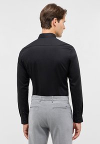 Zwarte langekousen shirt met een puntige kraag, gecombineerd met lichtgrijze broek met achterzakken en een gladde textuur.