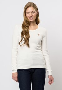 Witte lange mouwen geribbelde shirt met een ronde halslijn en een klein geborduurd detail op de linkerkant van de borst, gecombineerd met donkerblauwe jeans.