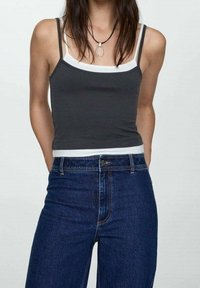 Débardeur noir avec bordure blanche, en tissu extensible. Associé à un jean en denim bleu taille haute avec une coupe droite et des coutures discrètes.