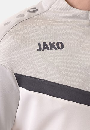 Lichtgrijs sportshirt met een gestructureerde bovenkant en een donkergrijze horizontale streep, met het prominent weergegeven "JAKO"-logo.