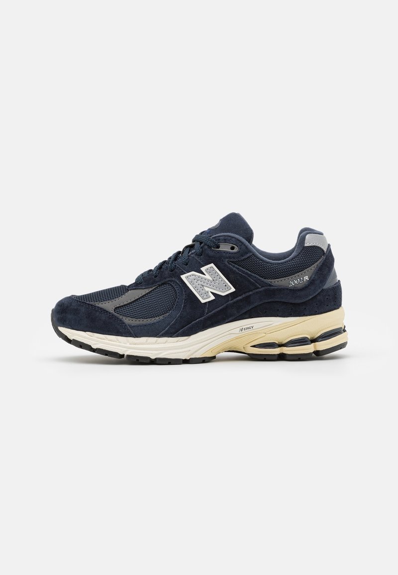 Baskets New Balance 2002R bleu marine avec dessus en mesh et suède, semelle blanche et beige, et logo réfléchissant sur le côté.