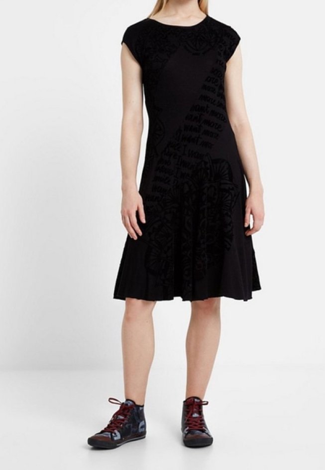 Femme portant une robe noire au genou avec des motifs subtils, associée à des baskets montantes foncées à lacets rouges.