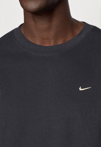 Σκούρο γκρι βαμβακερό t-shirt με στρογγυλή λαιμόκοψη, με μικρό χρυσό λογότυπο Nike στην αριστερή πλευρά του στήθους. Ομαλή υφή.