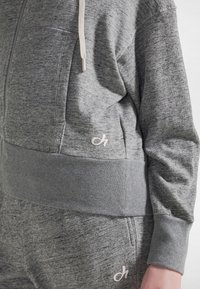 Felpa grigia con zip realizzata in tessuto strutturato, con orlo e polsini a costine, con un piccolo logo bianco sulla tasca laterale.