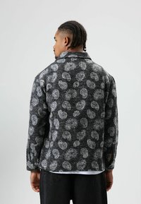 Zwart- en grijsgepatenteerd jack met een zachte textuur, voorzien van een kraag en lange mouwen, ontworpen met spiraalachtige accenten door het hele kledingstuk.