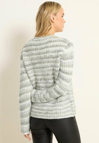 Grau-weiß gestreifter Pullover mit strukturiertem Strickdesign, rundem Ausschnitt und langen Ärmeln, kombiniert mit schwarzen, eng anliegenden Hosen.