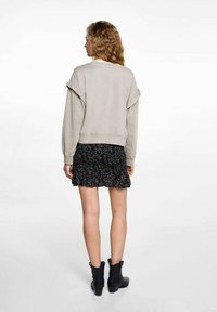 Svijetlosivi dukserica s labavim rukavima kombinira se s crnom suknjom sa cvjetnim uzorkom i volanima. Crne čizme do gležnja upotpunjuju outfit.