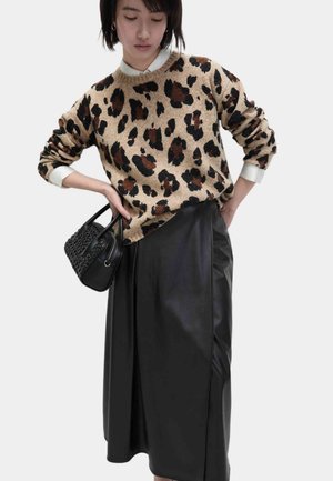 Beiger Pullover mit schwarzen und braunen Leopardenflecken, kombiniert mit einem schwarzen Lederrock. Zusätzliches Detail: kleine schwarze Handtasche mit gewebter Textur.
