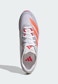 Białe buty sportowe z czerwonymi i pomarańczowymi paskami, białymi sznurowadłami oraz czerwonym logo na języku i wkładce, pokazane z góry na jasnym tle.