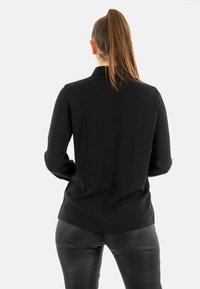 Maglietta nera a maniche lunghe con taglio dritto, realizzata in tessuto morbido, con orlo leggermente curvato e maniche con polsini.