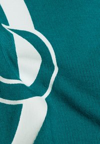 Tealstickad tyg har en framträdande vit abstrakt design och visar en texturerad yta med ett subtilt ribbat mönster.