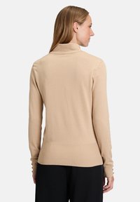 Pull en maille côtelée beige avec un col montant, design ajusté et boutons aux poignets ; texture lisse et style minimaliste.