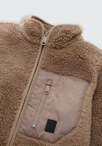 Beige fleece jas met een hoge kraag, voorrits en een soepele stoffen borstas met een verticale rits en zwart merklogo.