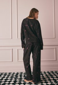 Set di pigiama nero con stampa leopardata viola, maniche lunghe e orlo arricciato sui pantaloni, progettato per il comfort con una vestibilità rilassata.